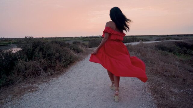 Mujer muy contenta sonriendo y dando vueltas de alegr&iacute;a mientras pasea por un camino de un parque natural al atardecer.