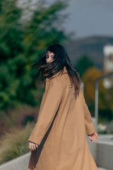 Young caucasian female in tan coat outdoors turning with long hair