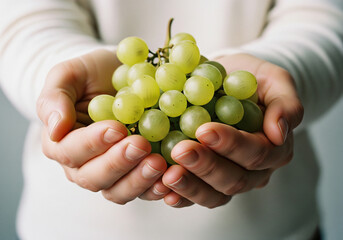 Gentle hands cradle a vibrant bunch of fresh green grapes, offering a taste of natural goodness and healthy living