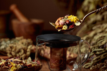 Various dried herbs and spices is poured into a glass teapot.