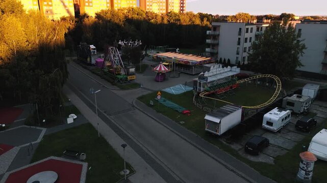 Niski przelot drona nad placem zabaw i karuzelą o poranku. Piękne pomarańczowe światło i bloki w tle.