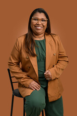 A smiling professional woman, wearing a brown blazer, green clothing, and glasses.