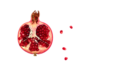 A cut open pomegranate reveals red seeds, with a few seeds scattered alongside, black background