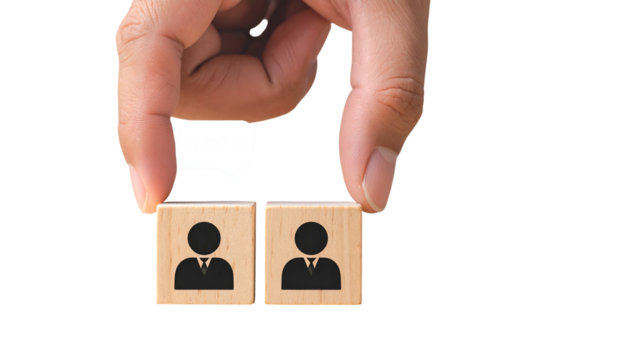 A hand holds two wooden blocks with person icons, conversation bubble above