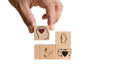 Hand placing a block with a heart within a head on a stack of wooden blocks
