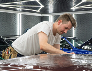 A specialist in wrapping a car with violet chameleon-colored vinyl film in the process of work. Car wrapping close-up. Car wrapping specialists cover the car with vinyl sheet or film. Selective focus.