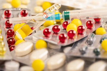 Multicolored tablets and capsules on the table. Ampoule and syringe for injections.