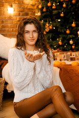 Beautiful curly girl in a white sweater with dark hair holds a garland of stars in her hands. New Year's portrait