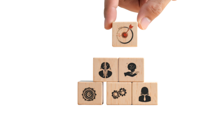 Hand placing a wooden block with target icon atop a pyramid of blocks with business icons