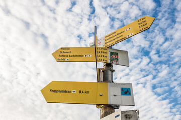 Wegweiser beim Krappenfelsen in den Weinbergen von Lauffen am Neckar mit Hinweis auf Neckarufer, Neckarwestheim, Schloss Liebenstein, Pfützen, Schozach und Ilsfeld vor blauem Himmel mit Wolken.