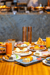 Luxurious breakfast buffet with diverse international dishes, juices, and pastries on wooden table in upscale restaurant dining setting.