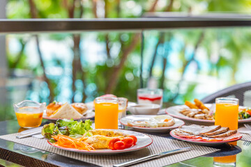 Tropical outdoor breakfast setting with fresh omelet, orange juice, fruit, pastries. Vibrant morning meal on patio, lush garden backdrop, ideal for travel, hospitality.