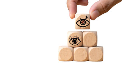 Hand adding wooden eye cube to pyramid of similar cubes on black, emphasizing vision & perspective