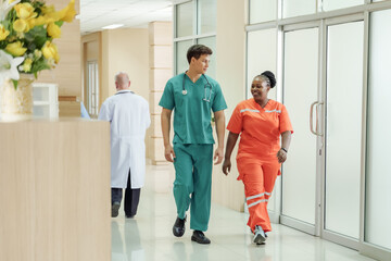 Multiracial medical team including male nurse and female emergency technician walking through hospital corridor in uniform smiling during shift change highlighting healthcare teamwork and readiness