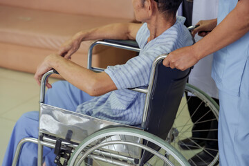 Obraz premium Closeup view of asian female nurse pushing senior asian male patient in wheelchair through hospital hallway, highlighting support, caregiving, and attentive healthcare service for recovery process
