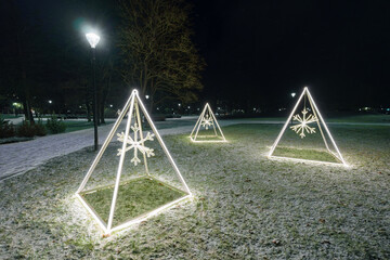 Minimalist Illuminated Christmas Pyramids with Snowflakes in Park on Dark Winter Night