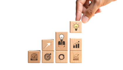 Hand places cube with lightbulb icon atop stacked wooden blocks, black background