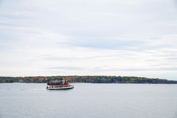 A passenger vessel cruises across Casco Bay with the shoreline’s fall foliage in the background, capturing the calm and colorful atmosphere of coastal Maine.