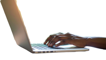 A dark-skinned person's hand typing on a laptop with the keyboard illuminated