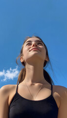 Naklejka premium Confident young woman with high ponytail looking up against blue sky
