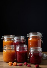 Homemade colorful fruit preserves displayed in glass canning jars. They sit on a wooden surface, suggesting traditional methods and care ,preservation ,vintage ,keeping