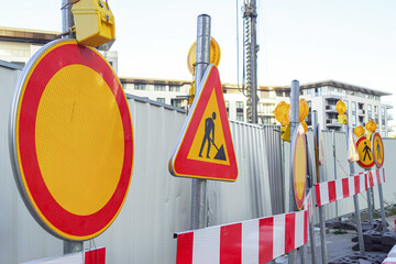 Construction warning signs with flashing lights lined along temporary metal fence. Represents urban infrastructure upgrade, roadwork safety measures, pedestrian protection, and city modernization.