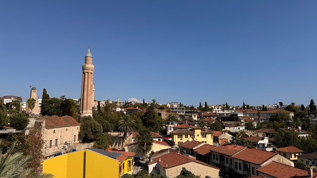 Panoramic view of Antalya's historic Kaleici district featuring the iconic fluted brick minaret Yivli Minare towering over traditional Ottoman-style houses under a clear blue sky.