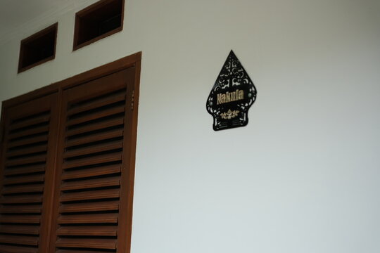 Intricate Nakula Wayang Shadow Puppet Decoration on White Wall beside Classic Wooden Door, a touch of Indonesian Culture and Heritage in interior