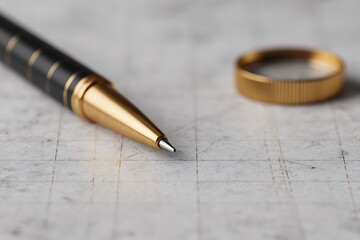 A sleek black and gold pen rests on a textured surface, accompanied by a golden ring, emphasizing elegance and precision in writing.