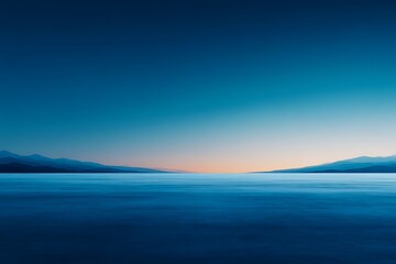 Tranquil seascape at dusk, featuring smooth water and layered mountains, with a gradient sky transitioning from deep blue to light hues.