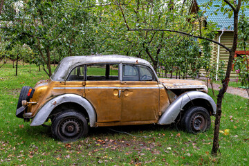 An old rusted car parked in a grassy area with trees in the background