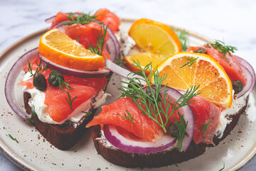 sandwich with freshly smoked salmon, on black bread, with cottage cheese, with herbs and red onions, capers and pieces of citrus fruits, on a marble countertop, breakfast, no people,