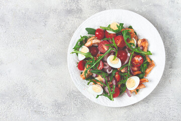 a warm salad with fried chicken fillet, arugula and cherry tomatoes, and boiled quail eggs, on a white plate, no people.