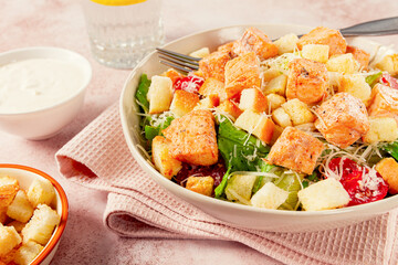 caesar salad with salmon, with croutons and dressing, in a salad bowl, on a pink table,