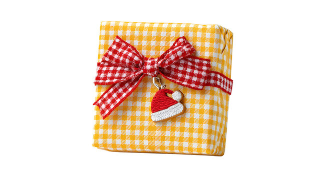 Playful gift in yellow gingham paper with red bow and illustrated Santa hat charm, cheerful pattern, isolated on white background