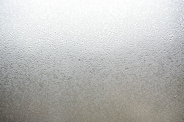 A photo of the glass surface of the window, covered with a multitude of droplets of various sizes. Background texture of a dense layer of condensate on glass