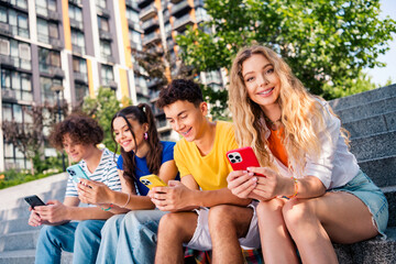 Group of cheerful teenagers bonding outdoors using smartphones and enjoying leisure time in a vibrant urban setting