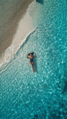 Woman swimming lying on her back in crystal clear turquoise water, top view from a height. Girl with a very beautiful face in a swimsuit enjoying beach vacation. Small ripples on turquoise water