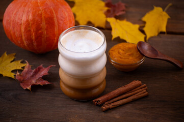 Cozy Autumn Pumpkin Spice Latte with Cinnamon Sticks, Pumpkin Butter, and Colorful Fall Leaves on Wooden Table