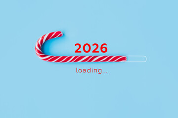 Striped candy cane and lettering 2026 loading on blue background. Concept of waiting for seasonal holidays