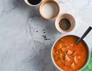 A bowl of soup is on a table with three other bowls and a spoon. The bowls are filled with different seasonings and spices, and the spoon is ready to be used. Concept of warmth and comfort
