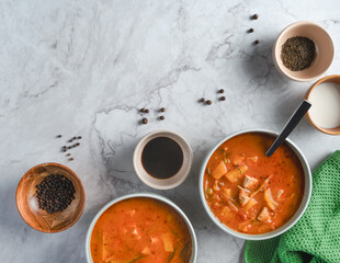 Two bowls of soup with a spoon and the spices in the small bowls on a marble counter. The bowls are filled with tofu tomato soup. The scene is inviting and cozy, with the bowls