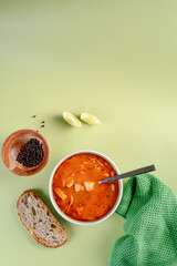 A bowl of vegan soup with a spoon and a slice of bread on a green background. The soup with tofu, tomato and zucchini. Dark green cloth on the side