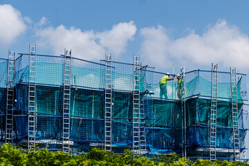 Construction Worker on Building Scaffold with Safety Netting, building development, industrial safety, labor, and the housing industry
