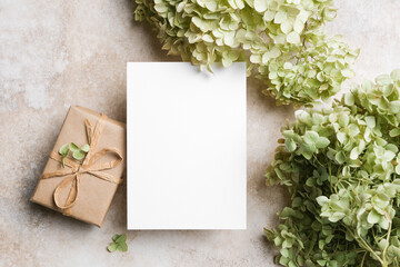 Vertical blank white greeting card mockup placed between green hydrangea flowers and a...