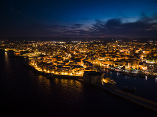 Night view of the illuminated historic center, harbor, and Carlo V Castle in Monopoli, Italy