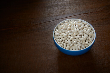 Tijela com feij&atilde;o branco cru, isolada em fundo de madeira