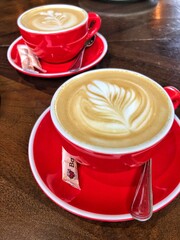 Close-up of a red ceramic cup of hot latte or cappuccino with beautiful foam art. Ideal for coffee shop menus, morning routine concepts, or beverage advertising.