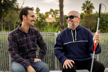 Blind Elderly Man with Glasses and Walking Stick Talking to His Caregiver on a Park Bench