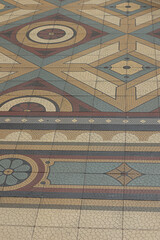 Detail of a vintage geometric tile floor with intricate patterns in beige, blue, red, and ochre tones, typical of 19th-century Portuguese architecture and interior design.